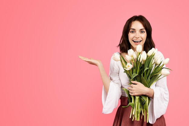 Uradowana emocjonalna młoda kaukaska dama w swobodnym stylu cieszy się prezentem w postaci bukietu kwiatów, pokazując rękę, aby zwolnić miejsce