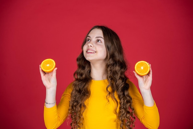 Uradowana nastoletnia dziewczyna trzyma pomarańczową owoc na purpurowym tle