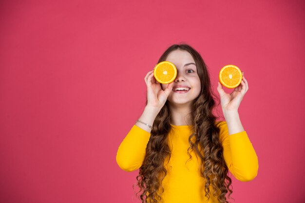 Uradowana nastoletnia dziewczyna trzyma pomarańczową owoc na różowym tle