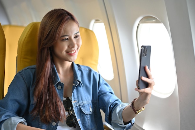 Urocza Azjatka używająca smartfona robiąca selfie Kobieta w samolocie