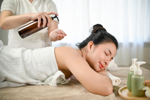 Urocza azjatycka kobieta leżąca na stole do masażu, otrzymująca olejek do masażu ciała na plecach i ramionach