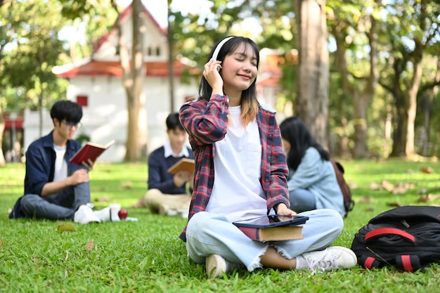 Urocza azjatycka kobieta lubi słuchać muzyki przez słuchawki, siedząc w parku