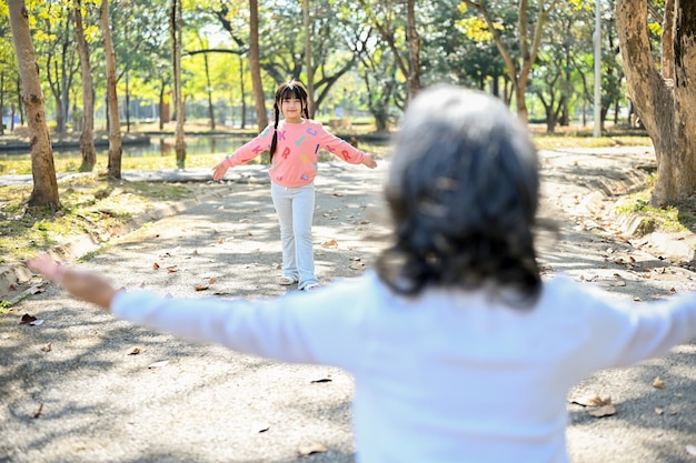 Urocza azjatycka wnuczka biegnąca do babci grająca w zabawną grę w parku