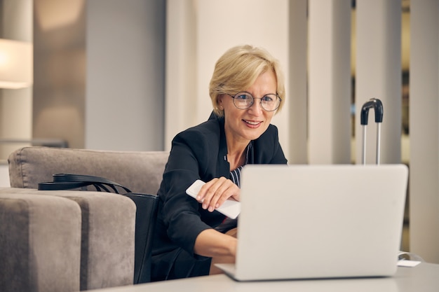 Urocza bizneswoman pracuje na laptopie i uśmiecha się, czekając na swój lot w holu