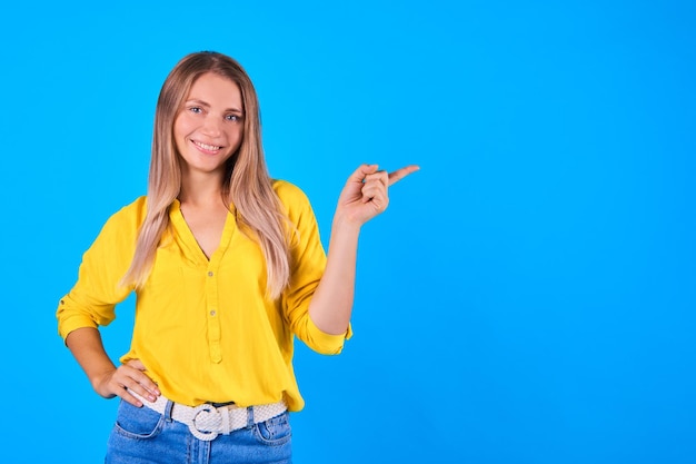 Urocza blondynka ubrana w przypadkowe ubrania, uśmiechająca się i wskazująca palcami, kopiować przestrzeń na białym tle