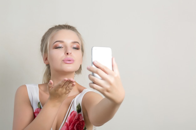 Urocza blondynka wysyła pocałunek powietrza i robi selfie na telefon komórkowy. Miejsce na tekst