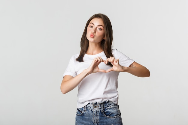 Urocza brunetka dziewczyna dąsa się do pocałunku i pokazuje gest serca