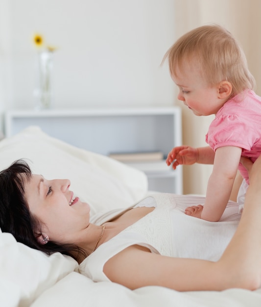 Urocza brunetki kobieta bawić się z jej dzieckiem podczas gdy kłamający na łóżku