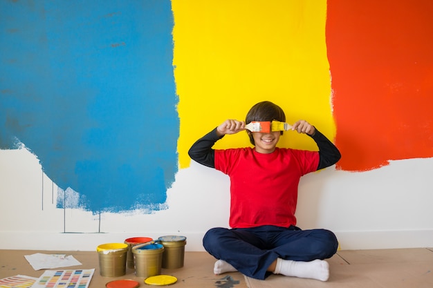 Urocza chłopiec w jaskrawej farbie z bałaganem farby dziecko na ścianie