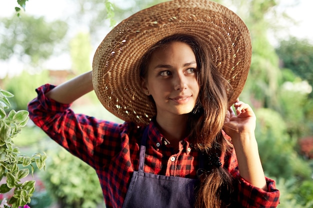 Urocza dziewczyna ogrodniczka w słomkowym kapeluszu stoi w cudownym ogrodzie w słoneczny dzień. .