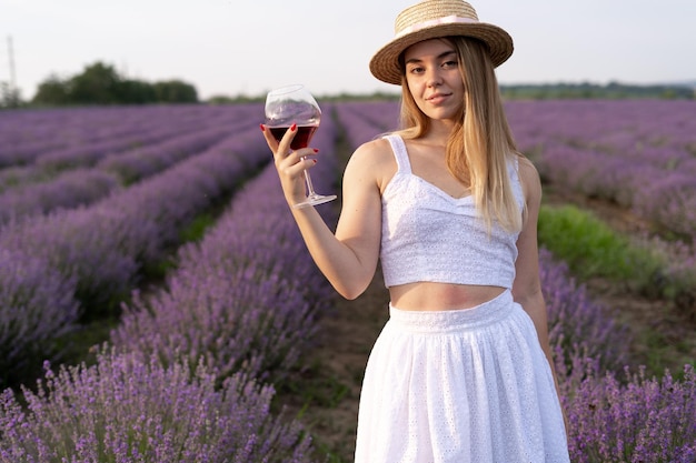 Urocza Dziewczyna Przy Lampce Czerwonego Wina W Lawendowym Polu W Letniej Prowansji. Alkohol W Naturze I Aromaterapia. Odpoczynek I Relaks Na świeżym Powietrzu. Odpoczywająca Pani Z Winem W Lawendzie