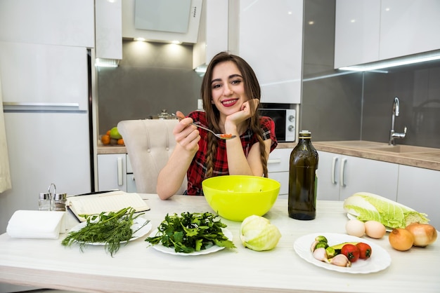 Urocza dziewczyna przygotowuje sałatkę z różnych warzyw i zieleni doprawioną oliwą z oliwek dla zdrowego stylu życia