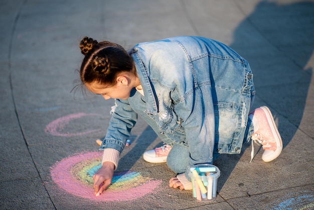 Urocza dziewczyna rysuje tęczę kredkami na ulicy Creation Kids Street