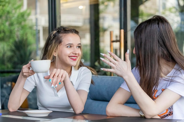 Zdjęcie urocza dziewczyna trzymająca kubek i rozmawiająca ze swoją przyjaciółką w restauracji