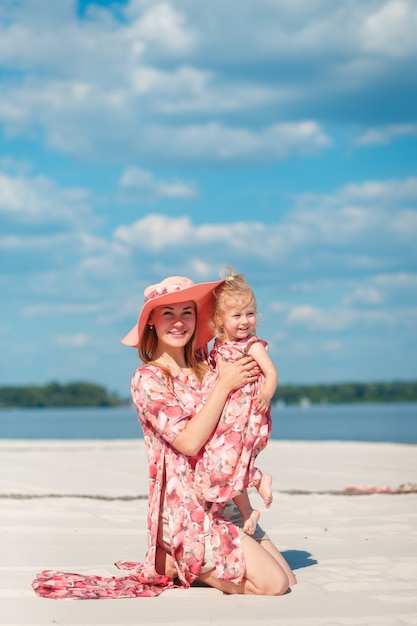 Urocza dziewczyna w lekkiej letniej sukience spaceruje po piaszczystej plaży z córeczką.