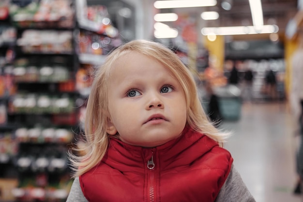 Urocza dziewczynka maluch siedzi w koszyku w sklepie lub supermarkecie Portret małe słodkie dziecko idzie na zakupy i kupowanie towarów na półce sklepowej