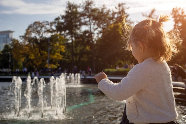 Urocza dziewczynka patrzy na malucha fontanna w parku z fontannami w słoneczny dzień rodziny