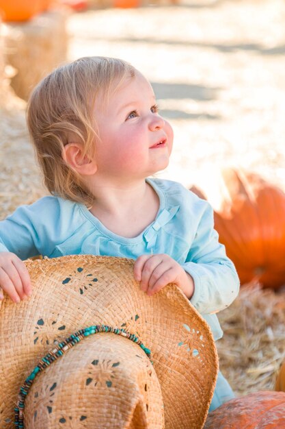 Urocza dziewczynka w kowbojskim kapeluszu w rustykalnym wiejskim otoczeniu na Pumpkin Patch