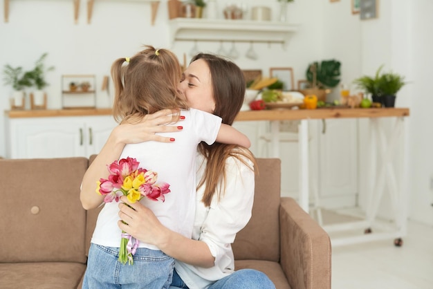 Urocza dziewczynka w wieku przedszkolnym daje bukiet kwiatów tulipanów podekscytowanej rodzinie mamy świętującej urodziny lub dzień matki