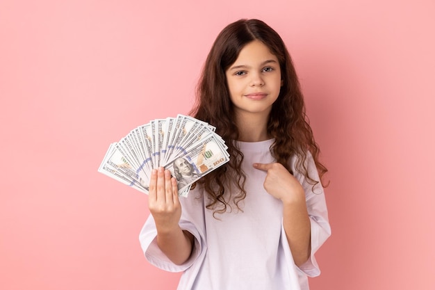 Urocza dziewczynka wskazująca na banknoty dolarów w dłoni, mająca spokojny wyraz twarzy, duży zysk