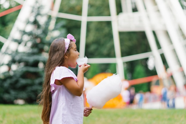 Urocza i ładna dziewczyna je białą słodką watę cukrową Szczęśliwe dziecko jedzące słodycze z emocjami w parku w lecie