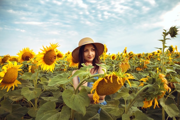 Urocza kobieta przechodzi przez żółty bukiet kwitnących słoneczników na świeżym powietrzu o wschodzie słońca, ciepłej naturze