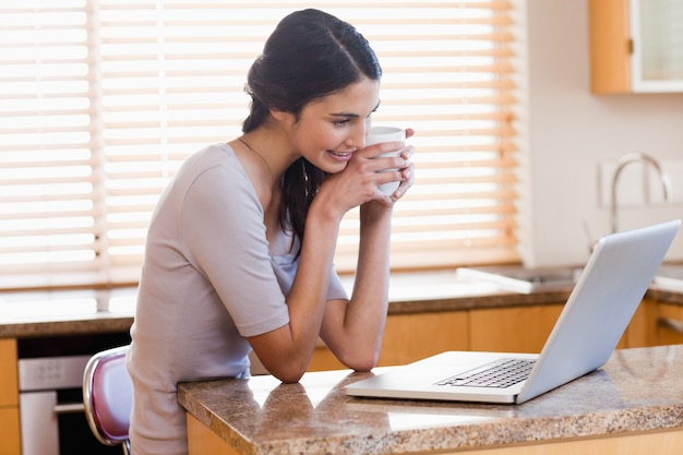 Urocza kobieta używa laptop podczas gdy pijący filiżankę kawa