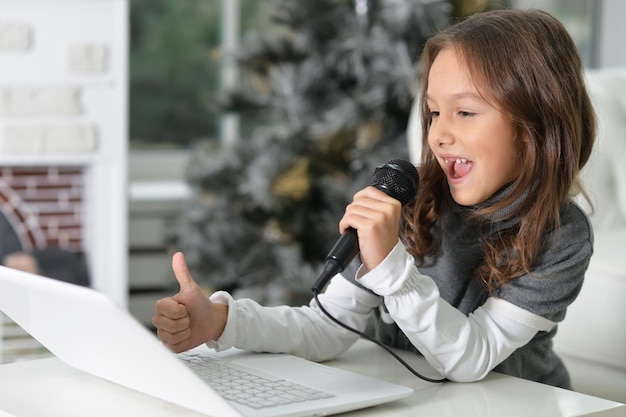 Urocza mała dziewczynka korzystająca z nowoczesnego laptopa i śpiewająca karaoke