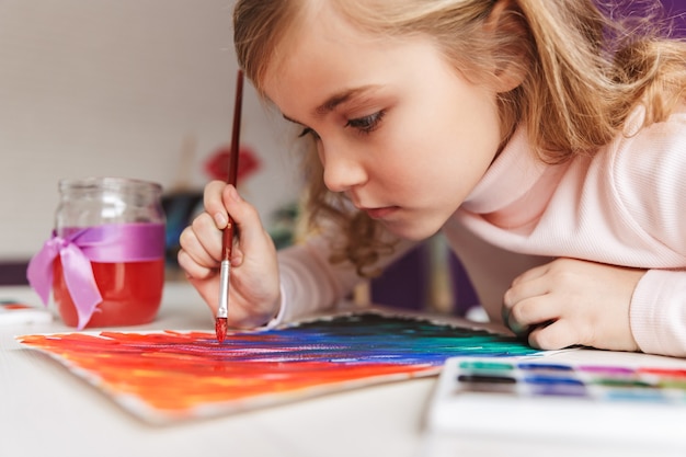 Urocza mała dziewczynka maluje obrazek przy stole w domu
