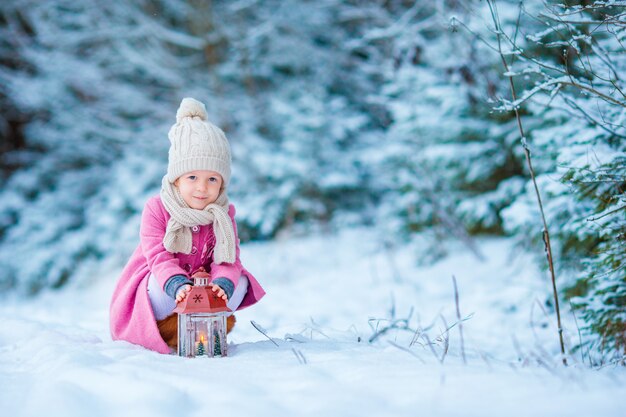 Urocza mała dziewczynka nosi ciepły płaszcz na zewnątrz w Boże Narodzenie ogrzewa zimne dłonie przez latarkę