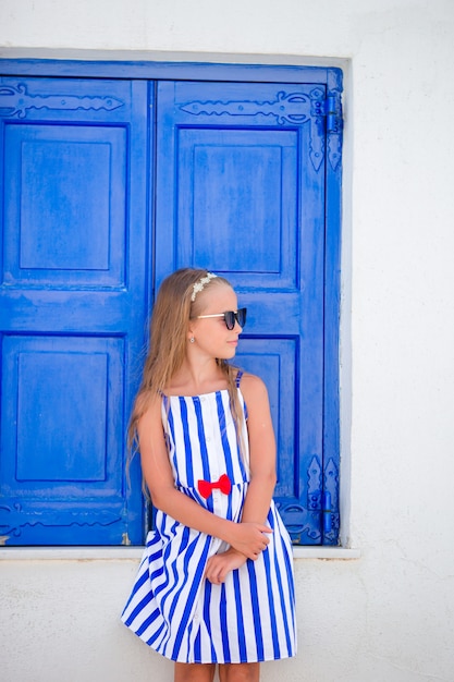 Urocza mała dziewczynka przed błękitnym drzwi outdoors przy typową grecką tradycyjną wioską na Mykonos w Grecja