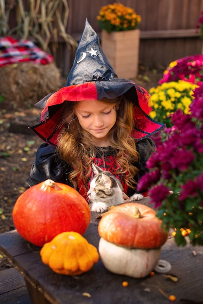 Urocza mała dziewczynka ubrana w kostium na halloween bawi się na plastrze dyni na pięknym jesiennym da