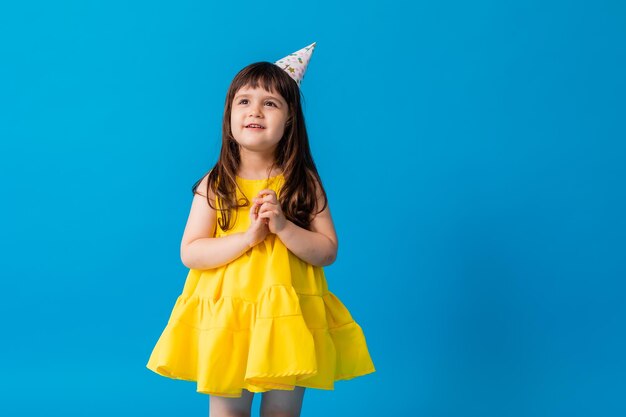 Urocza mała dziewczynka w żółtej sukience na niebieskim tle rzuca kolorowym konfetti Urodziny