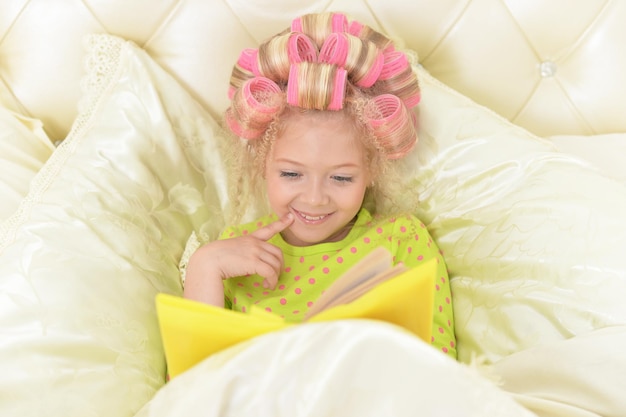 Urocza mała dziewczynka z różowymi lokówkami czyta