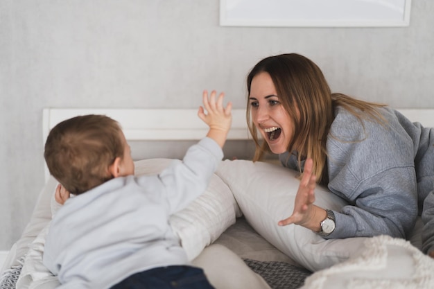 Urocza mama i jej synek bawią się w domu na łóżku w przytulnej sypialni