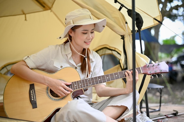 Urocza młoda Azjatka odpoczywa i drży podczas gry na gitarze w swoim namiocie kempingowym