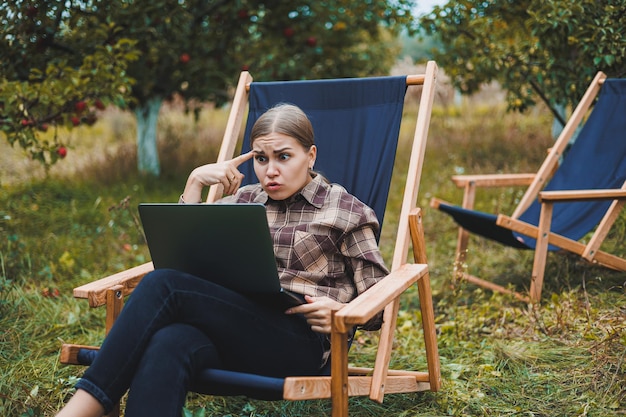 Urocza Młoda Freelancerka Pracuje W Ogrodzie Na świeżym Powietrzu, Siedząc Na Wygodnym Krześle Ogrodowym Praca Zdalna Na Przenośnym Laptopie