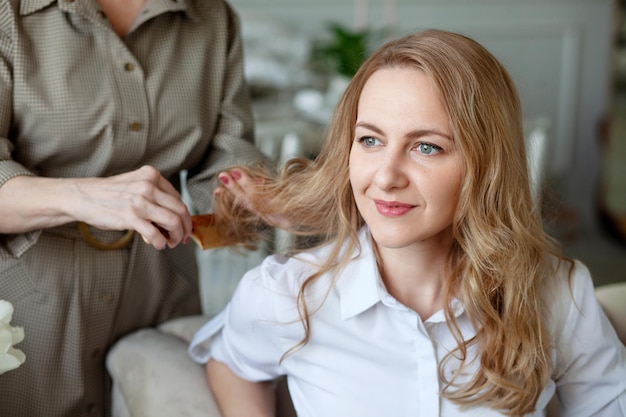 Urocza młoda kobieta uśmiecha się, gdy jej piękna mama czesze córce włosy Świetny związek między dorosłą córką a matką