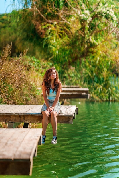 Urocza młoda kobieta w spódnicy siedzi na drewnianym moście na tle natury