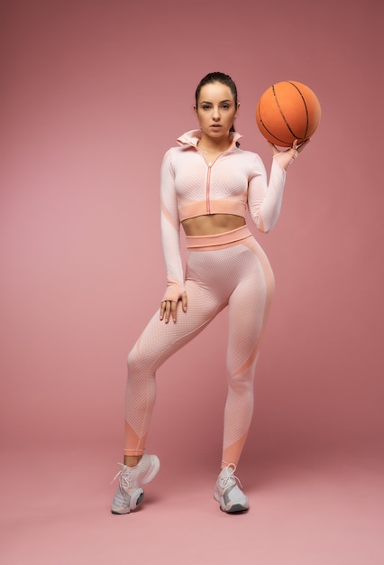 Urocza młoda kobieta z piłką do koszykówki stojącą w studio