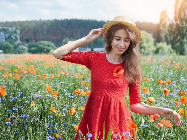 Urocza młoda romantyczna kobieta w słomianym kapeluszu na makowym kwiatu polu