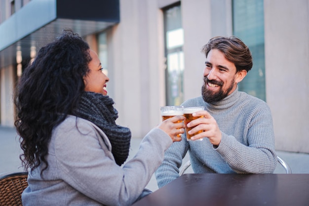 Urocza młoda wieloetniczna para wznosząca toast i pijąca piwo w miejskim barze, ciesząca się swoim wolnym czasem Koncepcja stylu życia
