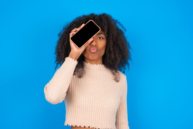 Urocza nastolatka pokazująca pusty ekranowy telefon i wskazująca palcami numer dwa