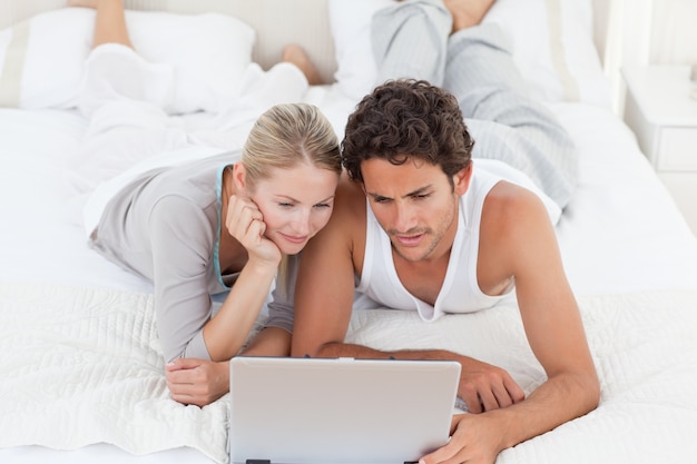 Urocza para patrzeje ich laptop na łóżku