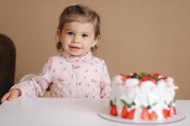 Urocza półtoraroczna dziewczynka stoi przy pysznym torcie urodzinowym Osiemnastomiesięczna dziewczynka jest bardzo szczęśliwa i śmieje się Jedzenie wegetariańskie Bez laktozy i glutenu