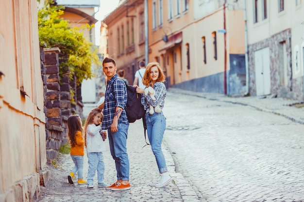 Urocza rodzina pełnych pasji podróżników stojących razem z córkami, patrzących w obiektyw na starożytnej ulicy miasta Użhorod na Ukrainie. Podróżowanie z koncepcją rodziny i dzieci