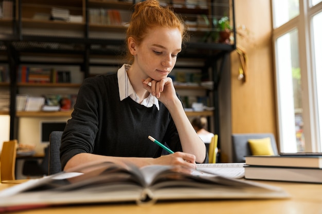 Zdjęcie urocza rudowłosa nastolatka studiuje przy stole