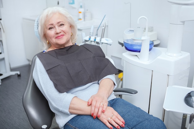 Urocza starsza kobieta uśmiechająca się do kamery, siedząca na fotelu dentystycznym w klinice