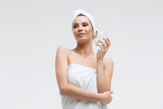 Urocza sympatyczna kobieta w puszystym białym ręczniku na głowie ze szklanką czystej wody odwracająca wzrok