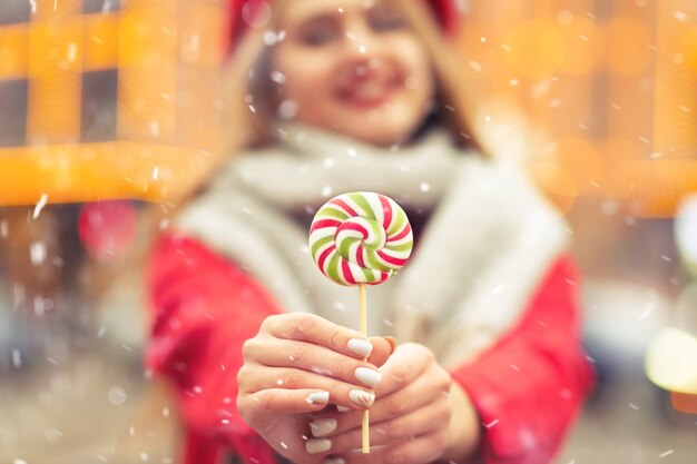 Urocza uśmiechnięta kobieta ubrana w płaszcz i ciepły szalik trzymający karmelowe cukierki podczas opadów śniegu